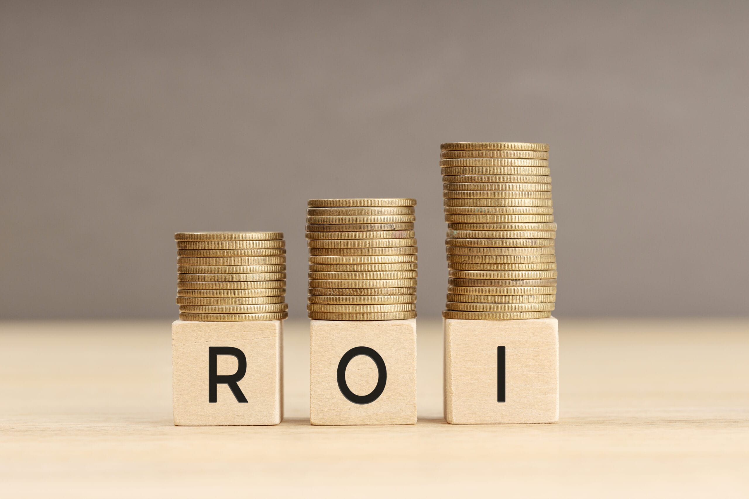 ROI word in wooden blocks with coins stacked in increasing stacks. Return on investment concept. Copy space