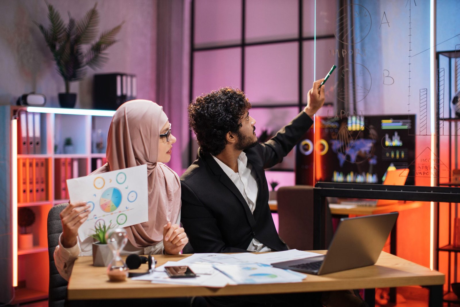 Smart bearded male office manager and muslim female businesswoman making financial report
